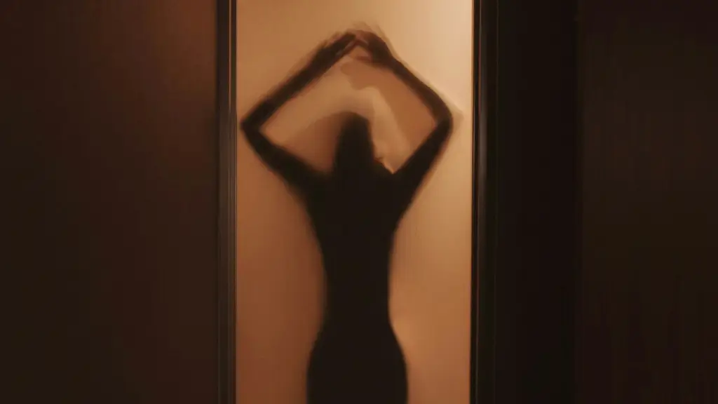 Una mujer desnuda parada frente a una ventana en una habitación oscura