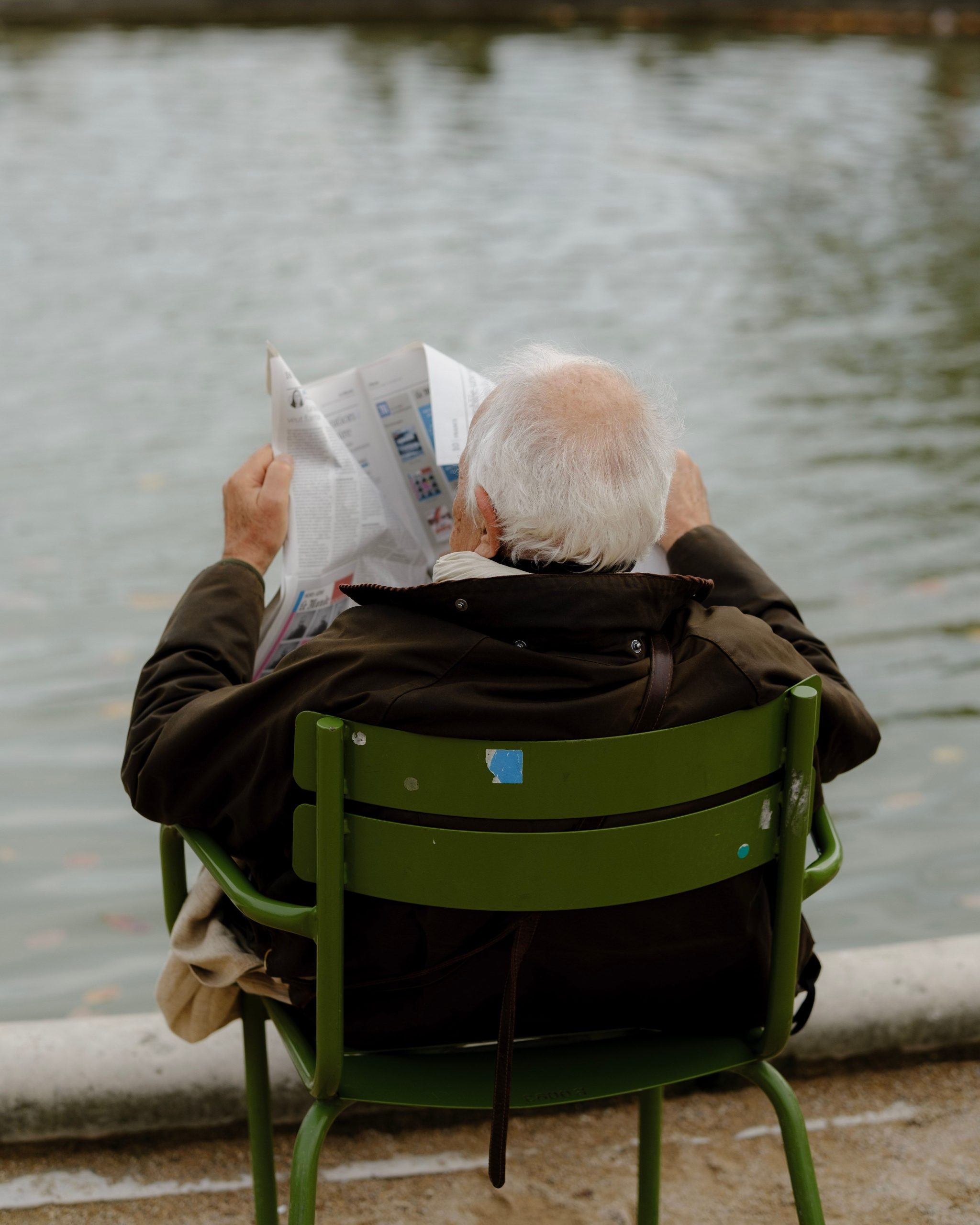 Una persona mayor sentada en una silla de jardín leyendo el periódico frente a un lago, ilustrando la tranquilidad financiera tras contratar un plan de pensiones para la jubilación.